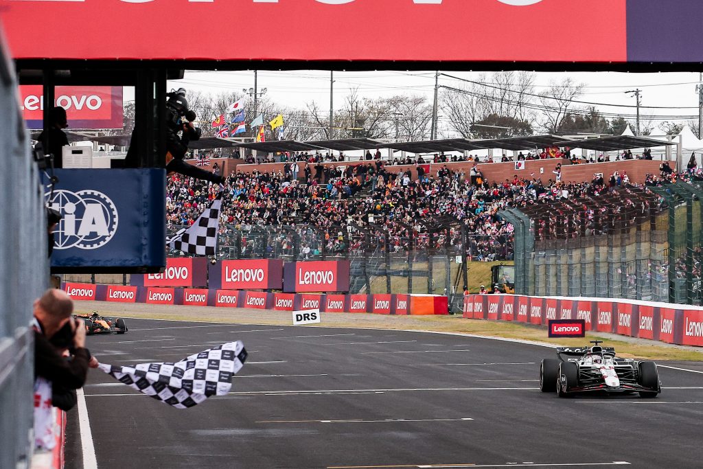 Max Verstappen’s Red Bull (dark blue car) #1 crosses the finish line to take the checkered flag, while a McLaren (orange car) follows further back on the straight.